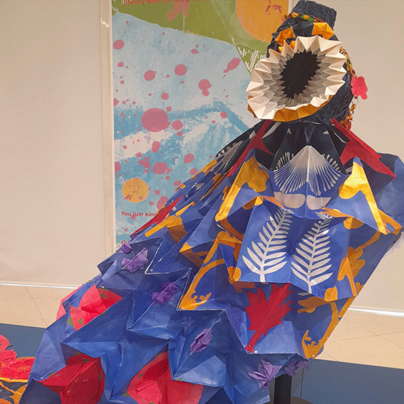 Blue origami paper dress with artistic cut out patterns against a pale background 